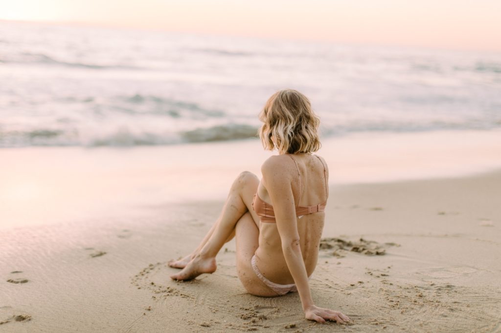girl sitting on sand looking at sunset for laguna beach boudoir session